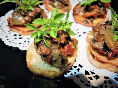 Toasted bread rounds topped with a vegetable mixture and fresh herbs, arranged on a lace doily.
