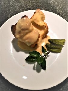 Chicken with creamy sauce on bread, garnished with pickles and a small sprig of greenery on a white plate.
