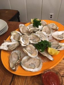 A platter of raw oysters on ice with lemon wedges and parsley, served on an orange tray next to a small bowl of sauce.