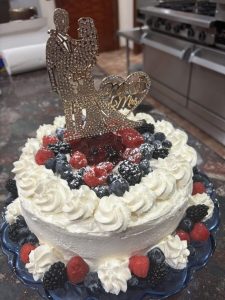 A decorated cake topped with berries, whipped cream, and a "Mr & Mrs" bride and groom silhouette topper.