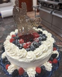 A decorated cake topped with berries, whipped cream, and a "Mr & Mrs" bride and groom silhouette topper.