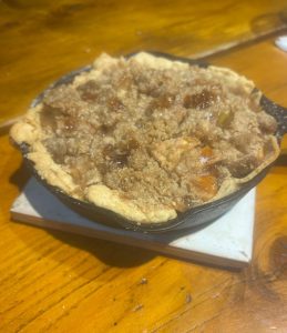 Mini apple crumble pie in a small cast iron skillet on a white tile, set on a wooden table.