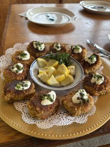 A platter of crab cakes topped with sauce and herbs, arranged around a bowl of lemon wedges on a gold plate.