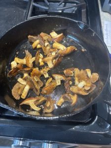 Chopped mushrooms cooking in a black cast iron skillet on a stovetop.
