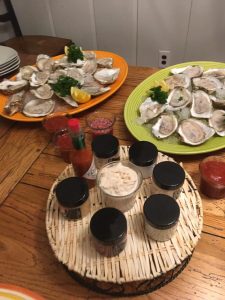 Two platters of raw oysters with lemon and parsley, assorted sauces, and condiments arranged on a wooden table.