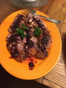 Sliced duck breast topped with a dark berry sauce and garnished with parsley on an orange plate.