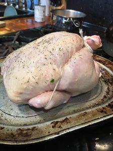 Raw whole chicken seasoned and trussed with twine on a baking tray, ready to be cooked in a kitchen setting.