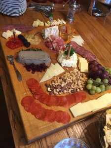 Charcuterie board with assorted cheeses, meats, nuts, crackers, grapes, berries, pâté, and spreads on a wooden table.