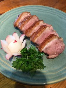 Sliced cooked duck breast served on a blue plate with parsley and a radish flower garnish.