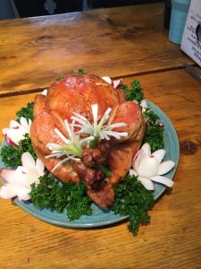 Whole roasted chicken on a green plate, garnished with parsley, radish flowers, and green onions on a wooden table.