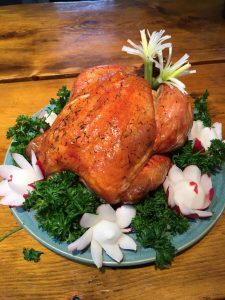 Roast chicken on a blue plate, garnished with parsley, radish flowers, and green onions, on a wooden table.