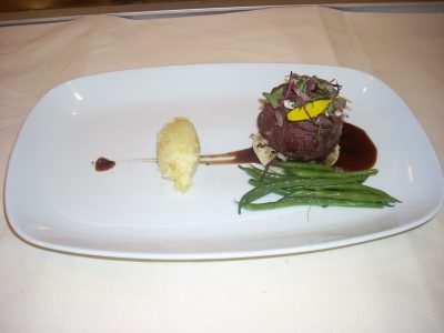 A plated meal with mashed potatoes, green beans, and a garnished steak with sauce on a white rectangular plate.