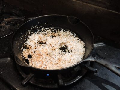 Shredded coconut being toasted in a black cast iron skillet on a gas stove.