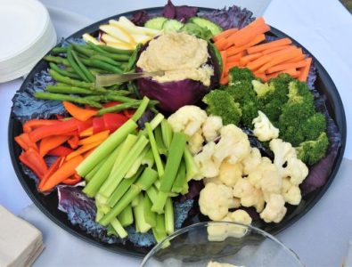A platter of assorted raw vegetables with a bowl of hummus dip in the center.