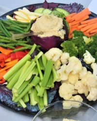 A platter of assorted raw vegetables with a bowl of hummus dip in the center.
