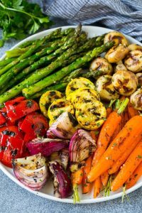 A plate of assorted grilled vegetables, including asparagus, mushrooms, carrots, onions, squash, and red bell peppers.