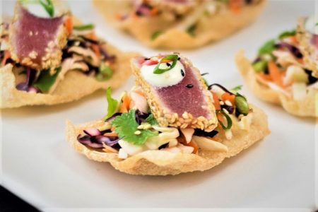 Sesame-crusted tuna slices with vegetables and sauce on crispy wonton chips, served as an appetizer on a white plate.