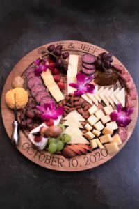A round charcuterie board with assorted cheese, meats, nuts, grapes, crackers, and purple orchids, dated October 10, 2020.