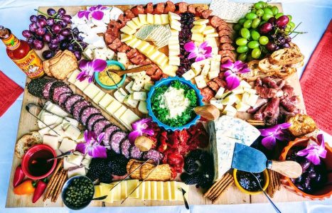 A large charcuterie board with assorted cheeses, meats, crackers, fruit, dips, bread, and edible flowers.