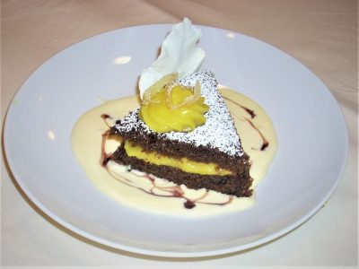 A slice of chocolate cake with yellow cream filling, powdered sugar, and whipped cream, served on a white sauce.